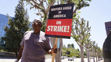 Dee Thompson, miembro del sindicato WGA y SAG-AFTRA, pasa junto a unos árboles árboles recién podados con un cartel en una manifestación frente a los estudios Universal el miércoles 19 de julio de 2023 en Burbank, California. (Foto AP/Chris Pizzello)
