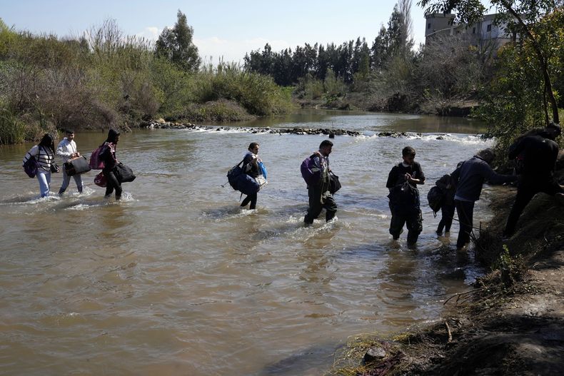 Familias sirias que huyeron de enfrentamientos en Siria cargan su equipaje al cruzar un río que marca la frontera entre Siria y el norte de Líbano, el martes 11 de marzo de 2025, en el poblado de Heker al-Daher, en la provincia de Akkar. (AP Foto/Hussein Malla)