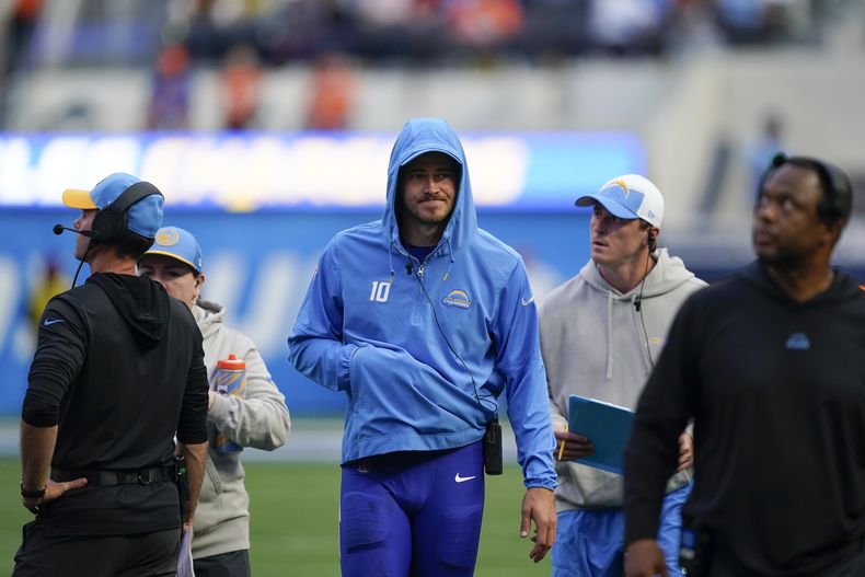 El quarterback de los Chargers de Los Ángeles Justin Herbert (centro) camina en las líneas laterales durante la segunda mitad, luego de una lesión en su mano que está dentro de su chaqueta, en el juego de la NFL ante los Broncos de Denver, el domingo 10 de diciembre de 2023, en Inglewood, California. (AP Foto/Ryan Sun)