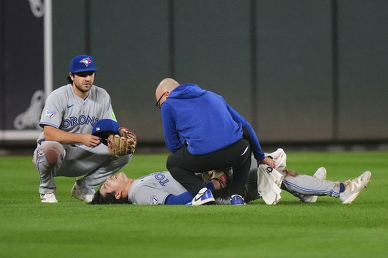 Brett Bateman, centro, jardinero central de los Azulejos de Toronto, yace tendido en el campo y es revisado por un asistente del equipo después de sufrir una lesión durante la segunda entrada del juego de béisbol de Grandes Ligas contra los Orioles de Baltimore, el lunes 21 de septiembre de 2026, en Baltimore. (AP Foto/Stephanie Scarbrough)