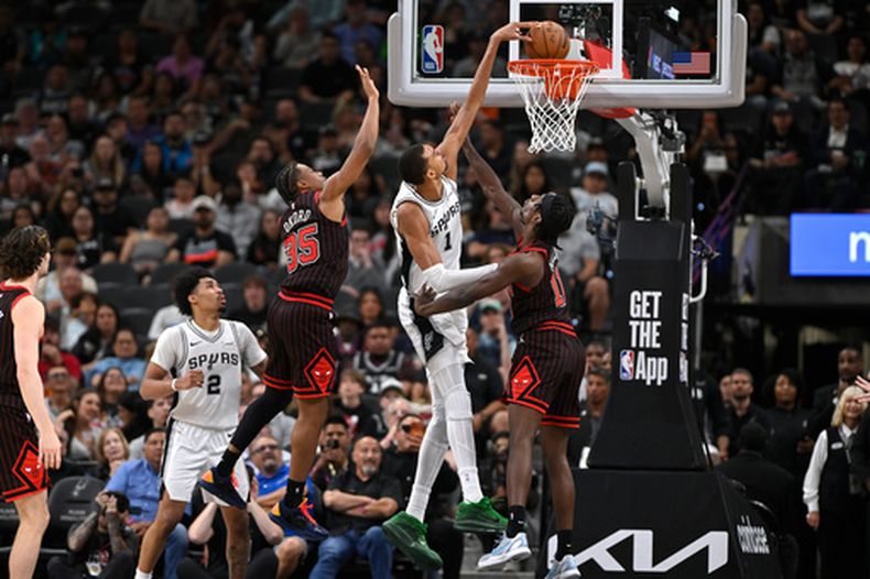 Victor Wembanyama (1), de los Spurs de San Antonio, retaca el balón entre Leonard Miller (11) e Isaac Okoro (35), de los Bulls de Chicago, durante la segunda mitad del juego de baloncesto de la NBA, el lunes 30 de marzo de 2026, en San Antonio. (AP Foto/Darren Abate)