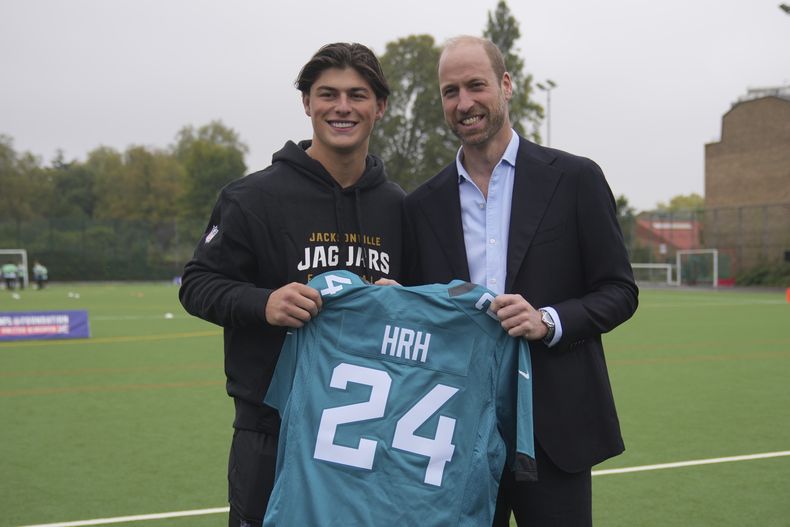 El Príncipe británico William, derecha, posa con Louis Rees-Zammit, sosteniendo un jersey mientras asiste a un evento de la NFL Foundation NFL Flag, un formato de fútbol americano inclusivo y de ritmo rápido, en Londres, el martes 15 de octubre de 2024. (Foto AP/Kin Cheung, Pool)