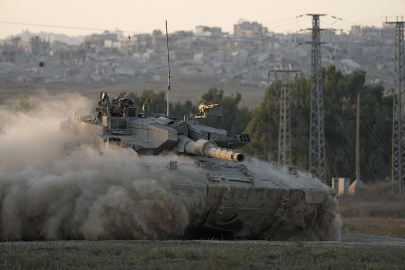Con edificios destruidos en Gaza de fondo, un soldado israelí saluda desde un tanque, cerca de la frontera entre Israel y Gaza, en el sur de Israel, el 1 de agosto de 2024. (AP Foto/Tsafrir Abayov)