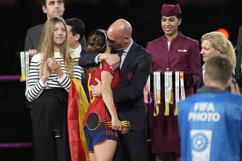 El presidente de la federación española de fútbol, Luis Rubiales (derecha) abraza a la volante Aitana Bonmatí en el podio tras la victoria de España ante Inglaterra en la final del Mundial femenino, el domingo 20 de agosto de 2023, en Sidney. A la izquierda aparece la infanta Sofía. (AP Foto/Alessandra Tarantino)