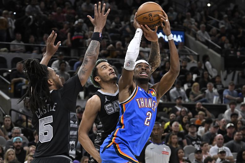 Shai Gilgeous-Alexander (2), del Thunder de Oklahoma City, ataca la canasta con la presión defensiva de Stephon Castle y Jeremy Sochan, de los Spurs de San Antonio, durante la primera mitad del juego de baloncesto de la NBA, el domingo 2 de marzo de 2025, en San Antonio. (AP Foto/Darren Abate)