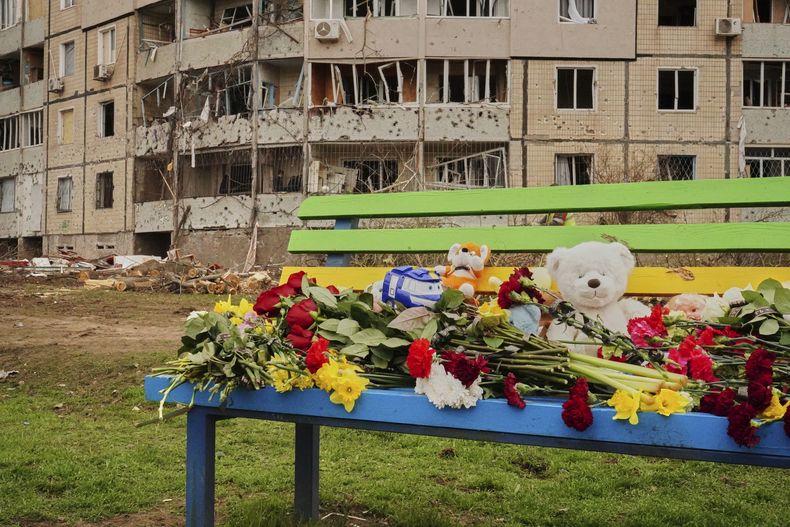 Flores y juguetes dejados en un banco para conmemorar a las víctimas muertas en el ataque con misiles de Rusia el viernes, en un área de juegos para niños cerca de los edificios de apartamentos dañados, en Kryvyi Rih, Ucrania, el sábado 5 de abril de 2025. (AP Foto)