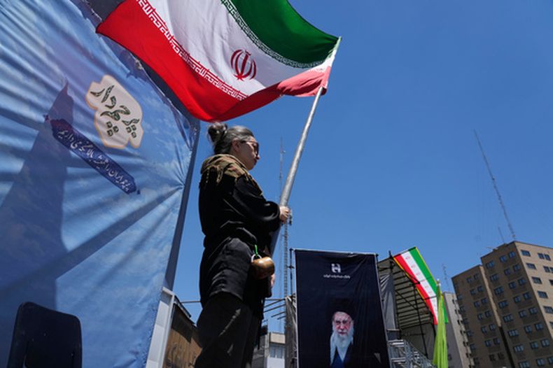 Una mujer ondea una bandera iraní durante una marcha progobierno, donde se ve la imagen del fallecido líder supremo iraní Alí Jamenei, asesinado en ataques de EEUU e Israel el 28 de febrero, en el centro de Teherán, Irán, el lunes 15 de junio de 2026. (AP Foto/Vahid Salemi)