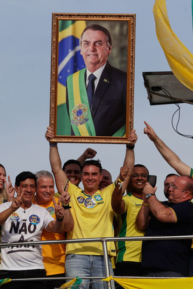 El candidato presidencial de oposición Flávio Bolsonaro sostiene una foto de su padre, el expresidente Jair Bolsonaro, mientras navega en un bote en un mitin de campaña previo a la elección general de octubre, en Angra dos Reis, en el estado de Río de Janeiro, Brasil, el sábado 29 de agosto de 2026. (AP Foto/Bruna Prado)