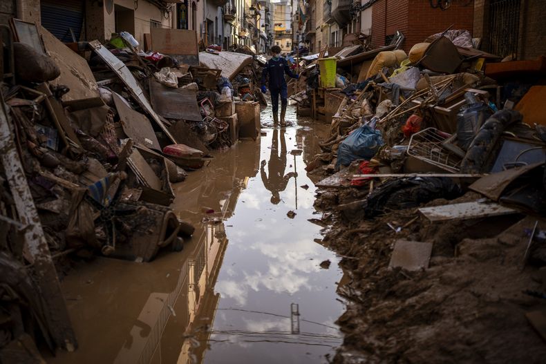 Una persona camina por la calle entre muebles y basura amontonada a los lados afectada por inundaciones en Paiporta, Valencia, España, el martes 5 de noviembre de 2024. (AP Foto/Emilio Morenatti)