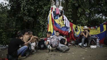 ARCHIVO - Migrantes sentados bajo un cartel que marca la frontera entre Panamá y Colombia durante su viaje a través del Tapón del Darién, el 9 de mayo de 2023. Abrumado por el resurgimiento de migrantes que cruzan la selva del Darién en la frontera con Colombia, el gobierno de Panamá anunció el jueves 24 de agosto de 2023 que tomará medidas concretas. (AP Foto/Iván Valencia, Archivo)