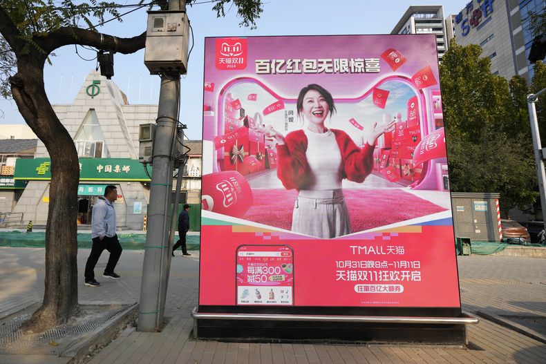 Transeúntes caminan junto a un anuncio que promueve un festival de ventas en Beijing, el martes 7 de noviembre de 2024. (AP Foto/Ng Han Guan)