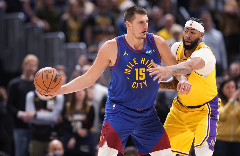 El serbio Nikola Jokic, pívot de los Nuggets de Denver, busca enviar un pase frente a Anthony Davis, alero de los Lakers de Los Ángeles, en el partido inaugural de la campaña de la NBA, el martes 24 de octubre de 2023 (AP Foto/David Zalubowski)