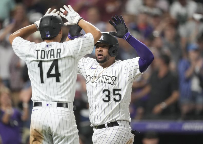 Ezequiel Tovar, izquierda, de los Rockies de Colorado, felicita a Elias Diaz popr su grand slam ante el relevista de los Angelinos de Los Ángeles Chris Devenski durante la octava entrada del juego de béisbol, el viernes 23 de junio de 2023, en Denver. (AP Foto/David Zalubowski)