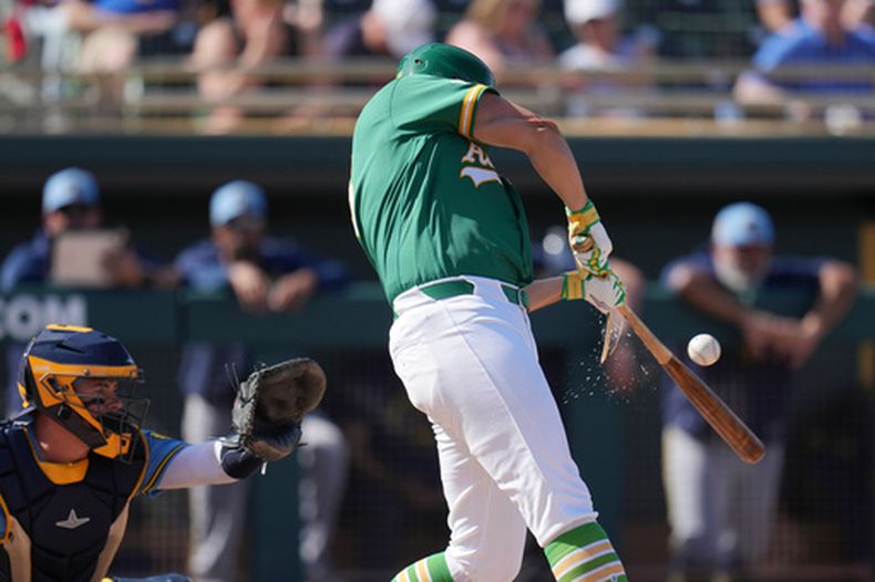 Nick Kurtz, derecha, de los Atléticos, rompe su bate al hacer contacto con la pelota, mientras Reese McGuire, izquierda, de los Cerveceros de Milwaukee, espera el lanzamiento durante la tercera entrada del juego de béisbol de los entrenamientos de primavera, el 24 de febrero de 2026, en Mesa, Arizona. (AP Foto/Ross D. Franklin)