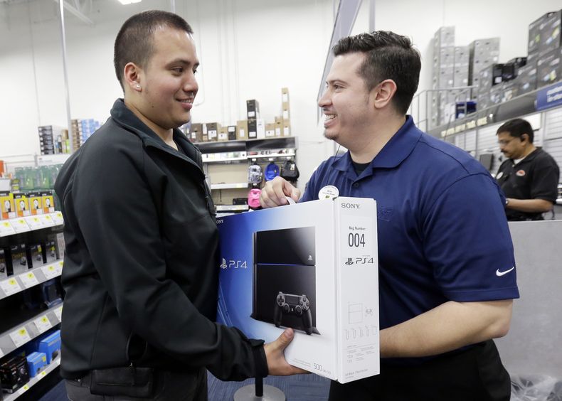 Andy Varadez (izquierda) recibe una consola PlayStation 4 de manos del gerente de Best Buy Michael Centeno luego de comprar el producto en la tienda de Best Buy en Lincoln Park, Chicago, el viernes 15 de noviembre de 2013. (Foto AP/Nam Y. Huh)