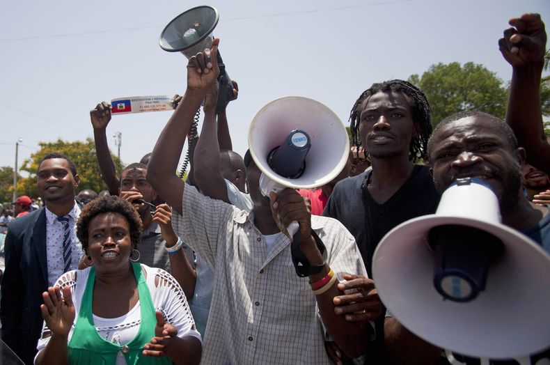 Manifestantes corean consignas contra Francia mientras el presidente francés Francois Hollande pronuncia un discurso frente al Palacio Nacional en Puerto Príncipe, Haití, el 12 de mayo de 2015. (AP Foto/Dieu Nalio Chery, File)