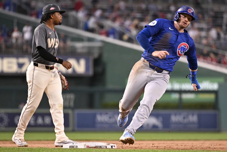 Ian Happ, derecha, de los Cachorros de Chicago, corre por delante de José Tena, tercera base de los Nacionales de Washington, para enfilarse a anotar con doble de Michael Busch durante la segunda entrada del juego de béisbol del viernes 30 de agosto de 2024, en Washington. (AP Foto/John McDonnell)