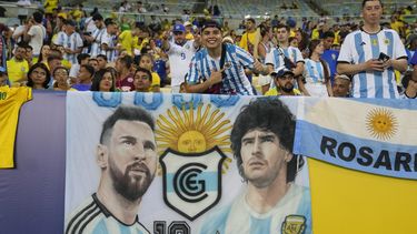 Hinchas alientan frente a una pancarta con la imagen del delantero argentino Lionel Messi y el fallecido astro Diego Maradona previo al partido entre Argentina y Brasil por las eliminatorias del Mundial, el martes 21 de noviembre de 2023, en Río de Janeiro (AP Foto/Silvia Izquierdo)