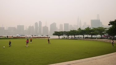Un grupo de personas juega en el Hunters Point South Park Athletic Field. Al fondo se aprecian los rascacielos de Nueva York, ocultos parcialmente por el humo de los incendios forestales en Canadá, el jueves 16 de julio de 2026 (AP Foto/Frank Franklin II)