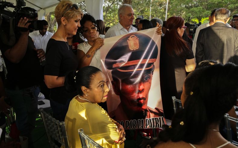 ARCHIVO - Iris Herrera, viuda del teniente Braulio Bethancourt Armstrong, esta sentada con sus hijas mientras una sostiene su fotografía durante una ceremonia en honor a los que murieron durante la invasión militar estadounidense de 1989 a Panamá en el cementerio Jardín de Paz en la Ciudad de Panamá, el 20 de diciembre de 2019. (AP Foto/Arnulfo Franco, Archivo)