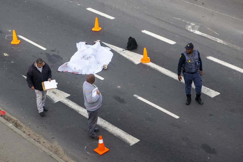 Policías acuden al lugar donde yace un cadáver cubierto en una calle en las afueras de Ciudad del Cabo, Sudáfrica, el lunes 7 de agosto de 2023. (AP Foto)