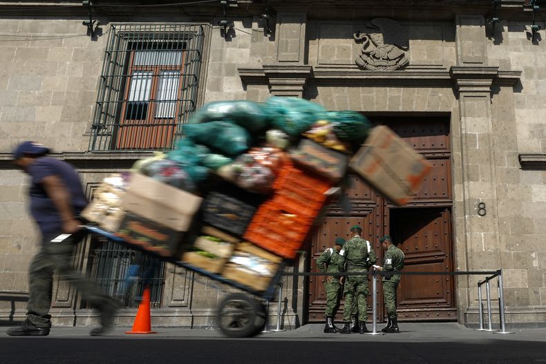 ARCHIVO - Un hombre tira un carrito lleno de mercancías frente al Palacio Nacional en la Ciudad de México, el 5 de diciembre de 2019. (AP Foto/Rebecca Blackwell, Archivo)