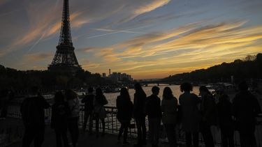 La gente admira el atardecer desde el puente de Debilly cerca de la torre Eiffel, el sábado 12 de noviembre de 2022, en París. (AP Foto/Michel Euler)