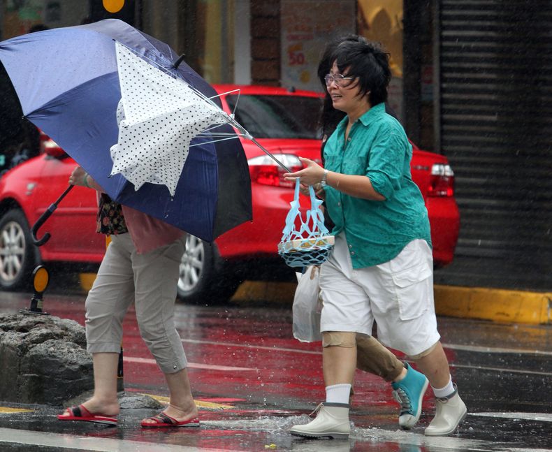 Ante los efectos del tif&oacute;n Fitow, mujeres llevan sus sombrillas, una de &eacute;stas vencida por el viento, en Taipei, Taiw&aacute;n, el domingo 6 de octubre de 2013. (AP Foto/Chiang Ying-ying)