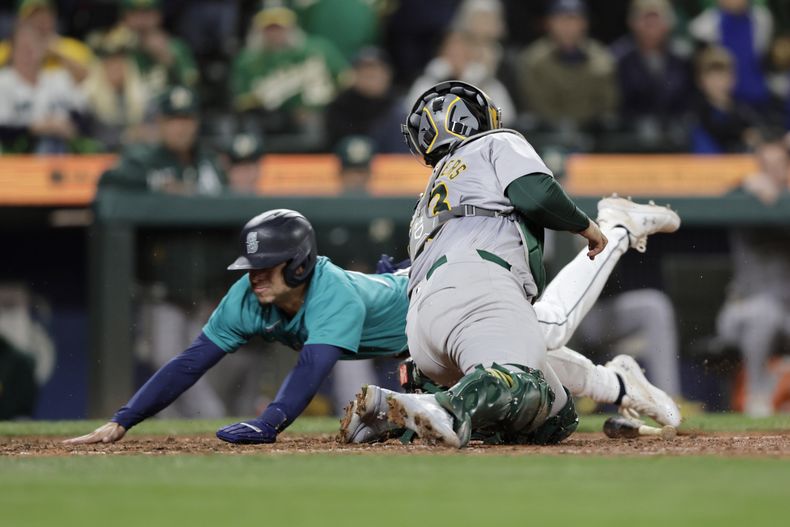 Leo Rivas, izquierda, de los Marineros de Seattle, anota carrera mientras el receptor de los Atléticos de Oakland, Shea Langeliers, intenta retirarlo con un toque en la décima entrada del juego de béisbol del sábado 28 de septiembre de 2024, en Seattle. Los Marineros ganaron 7-6. (AP Foto/John Froschauer)