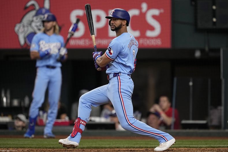 Leody Taveras, derecha, de los Rangers de Texas, sigue con la mirada un sencillo con el que produjo una carrera en contra de los Rays de Tampa Bay en la quinta entrada del juego de béisbol del domingo 7 de julio de 2024, en Arlington, Texas. Wyatt Langford anotó en la jugada. (AP Foto/Tony Gutierrez)