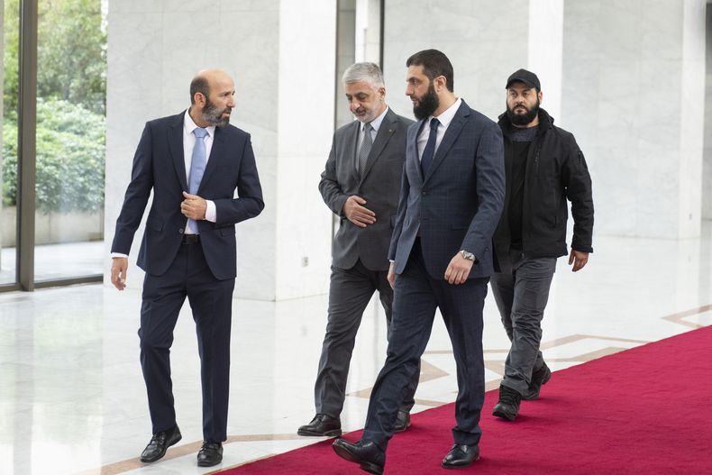 El líder de facto de Siria, Ahmad al-Sharaa, al frente, conocido anteriormente como Abu Mohammed al-Golani, camina en el palacio presidencial antes de reunirse con Walid Ellafi, ministro libio de comunicación y asuntos políticos, en Damasco, el sábado 28 de diciembre de 2024. (AP Foto/Mosaab Elshamy)