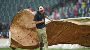 Un miembro del equipo de protección del campo de juego coloca una lona sobre el montículo para protegerlo de la lluvia durante un partido de béisbol de Grandes Ligas entre los Orioles de Baltimore y los Filis de Filadeflia que fue postergado por el clima, el domingo 2 de agosto de 2026, en Baltimore. (AP Foto/Stephanie Scarbrough)