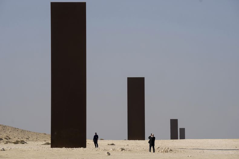 ARCHIVO - Personas miran la pieza East-West/West-East del artista estadounidense Richard Serra en una sección desolada de la Reserva Natural de Brouq, en la parte noroeste del desierto del país, cerca de Zekreet, Qatar, el 3 de diciembre de 2022. Serra, conocido por convertir paredes curvas de acero oxidado y otros materiales maleables en obras de arte a gran escala que ahora están repartidas por todo el mundo, murió el martes 26 de marzo de 2024 en su casa en Long Island, Nueva York. Tenía 85 años. (Nathan Denette/The Canadian Press via AP, archivo)
