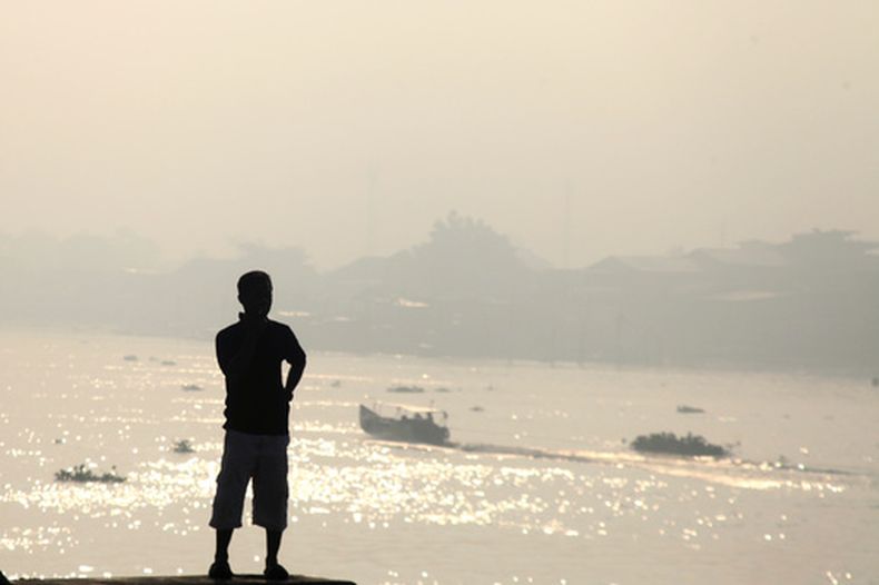 Un hombre observa la bruma de los incendios forestales que cubre el río Musi en Palembang, Sumatra Meridional, Indonesia, el domingo 23 de agosto de 2026. (Foto AP/Muhammad Fajri)