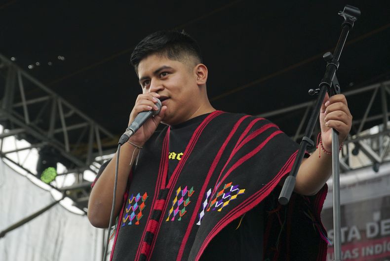 El rapero mexicano-triqui Carlos CGH, vestido con un gabán negro y rojo, una prenda nativa del pueblo triqui en el oeste de Oaxaca, actúa durante una celebración de los pueblos indígenas en el Zócalo de la Ciudad de México, el martes 6 de agosto de 2024. (Foto AP/Mariana Martínez Barba)