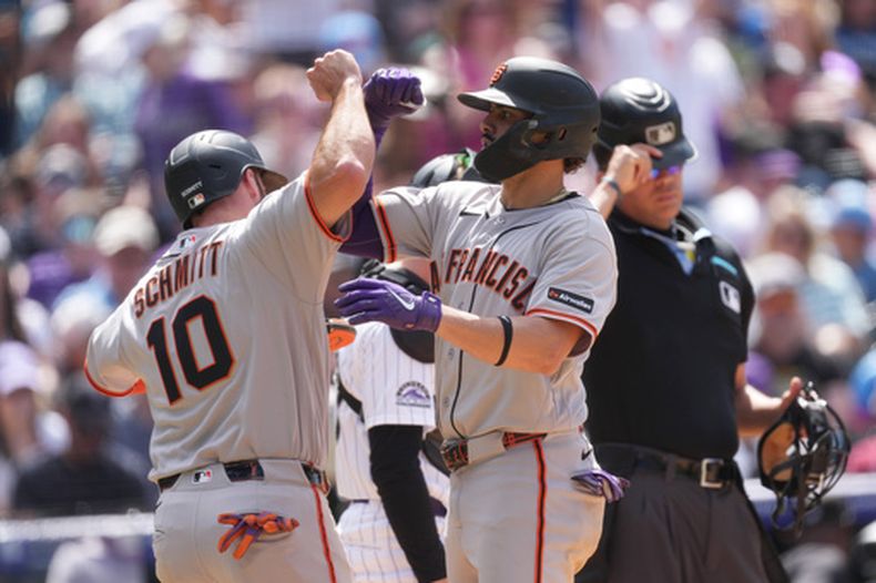Casey Schmitt, izquierda, de los Gigantes de San Francisco, celicita a Willy Adames, centro, mientras cruza el plato después de disparar un grand slam ante el relevista de los Rockies de Colorado, Zach Agnos, en la quinta entrada del juego de béisbol de Grandes Ligas, el domingo 31 de mayo de 2026, en Denver. (AP Foto/David Zalubowski)