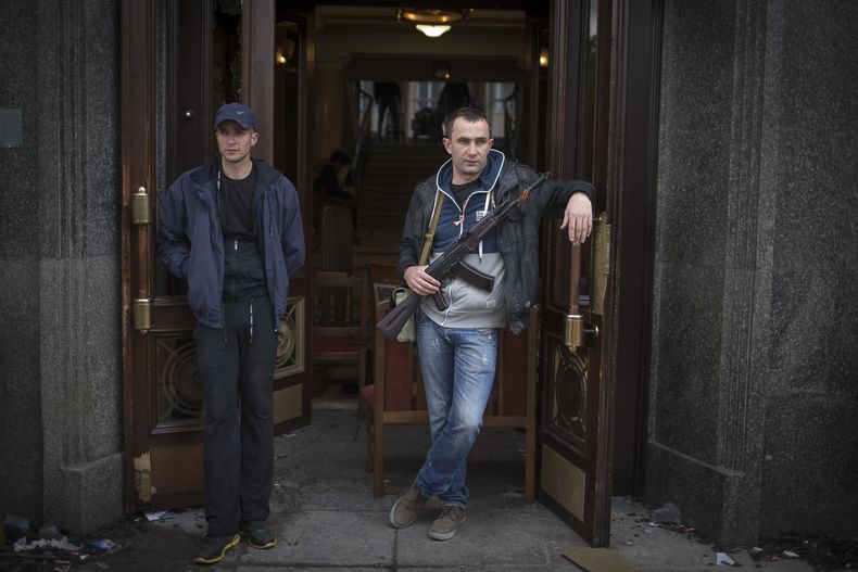 Activistas pro rusos, uno de los cuales sostiene un fusil autom&aacute;tico Kalashnikov, resguardan la entrada de un edificio del gobierno tomado en el centro de la ciudad de Luhansk, Ucrania, una de las mayores ciudades asoladas por las actividades de lo