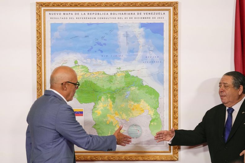 El presidente de la Asamblea Nacional, Jorge Rodríguez (izquierda), y el presidente de la Comisión Especial para la Defensa de Guyana Esequiba, Hermann Escarra, se dan la mano después de revelar el nuevo mapa de Venezuela que incluye el territorio del Esequibo, una franja de tierra administrada y controlada por Guyana pero reclamada por Venezuela, en Caracas, Venezuela, el viernes 8 de diciembre de 2023. (Foto AP/Matías Delacroix)