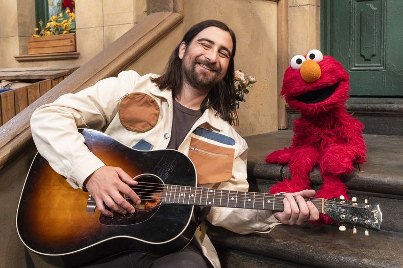 Esta imagen proporcionada por Sesame Workshop muestra al cantante Noah Kahan, a la izquierda, con el personaje de los muppets Elmo en el set de Sesame Street. (Zach Hyman/Sesame Workshop vía AP)