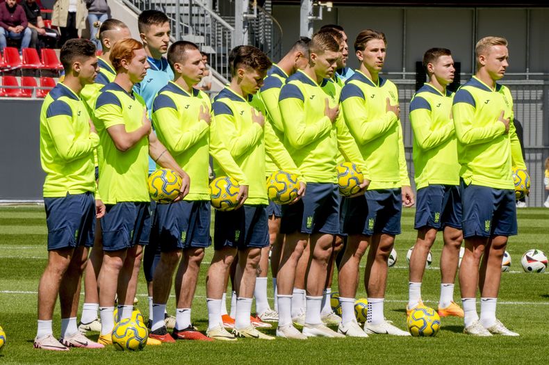 Futbolistas de la selección nacional de Ucrania escuchan el himno nacional durante una sesión de entrenamientos abierta al público, en Wiesbaden, Alemania, el jueves 13 de junio de 2024, preparándose de cara al partido ante Rumania, en la Eurocopa 2024. (AP Foto/Michael Probst)