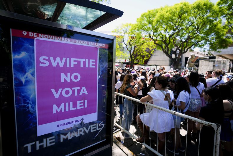 Fanáticos de Taylor Swift esperan en la entrada del Estadio Monumental donde la cantante dará su primer concierto de The Eras Tour, en Buenos Aires, Argentina, frente a un cartel que se refiere al candidato presidencial Javier Milei, el jueves 9 de noviembre de 2023. (AP Foto/Natacha Pisarenko)