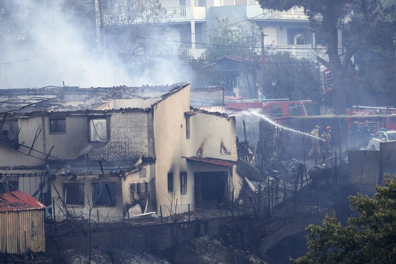 Bomberos trabajan para extinguir un incendio en una casa durante un incendio forestal en el suburbio noroccidental de Kryoneri, en Atenas, Grecia, el sábado 26 de julio de 2025. (AP Foto/Yorgos Karahalis)