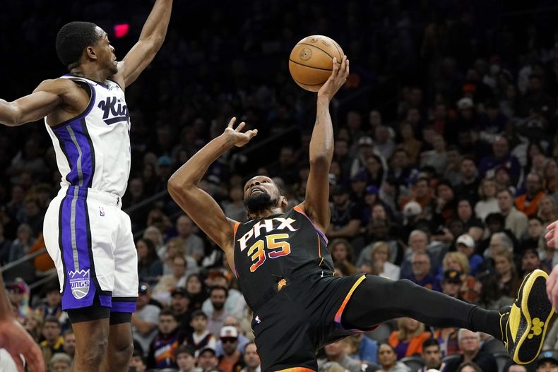 Kevin Durant, alero de los Suns de Phoenix, dispara frente a DeAaron Fox, de los Kings de Sacramento, durante el duelo del martes 16 de enero de 2024 (AP Foto/Ross D. Franklin)
