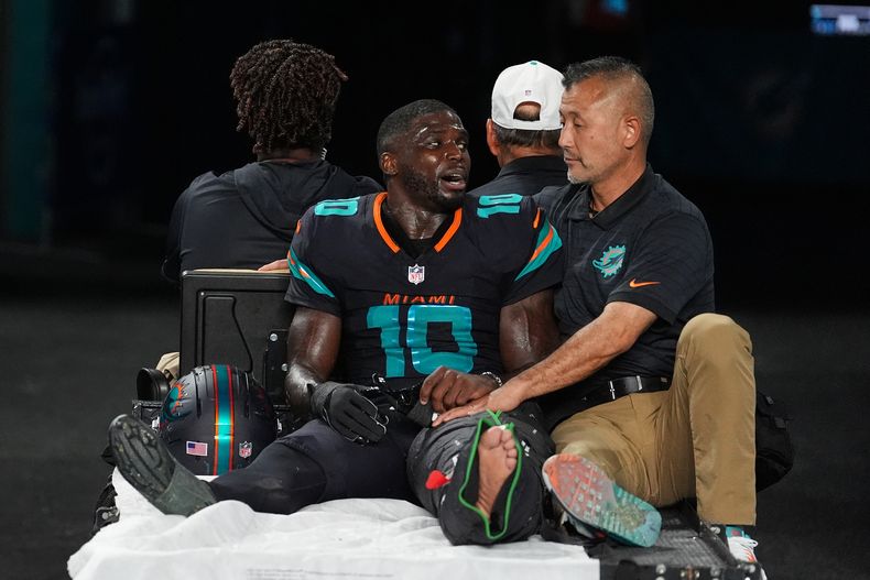 Tyreek Hill (10), wide receiver de los Dolphins de Miami, habla con un asistente médico del equipo mientras es trasladado en el carrito fuera del campo después de sufrir una lesión en la rodilla izquierda durante el partido de la NFL contra los Jets de Nueva York, el lunes 29 de septiembre de 2025, en Miami Gardens, Florida. (AP Foto/Rebecca Blackwell)