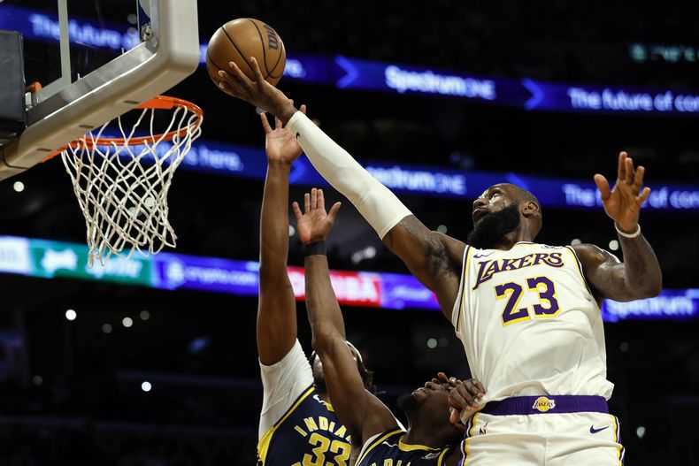El alero de los Lakers de Los Ángeles LeBron James lanza el balón sobre el pívot de los Pacers de Indiana Myles Turner y el alero Aaron Nesmith en el encuentro del domingo 24 de marzo del 2024. (AP Foto/Etienne Laurent)