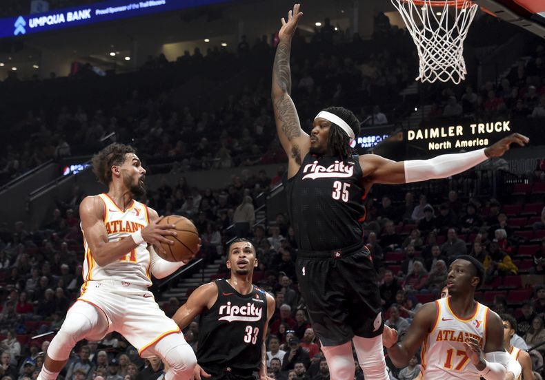 El escolta de los Hawks de Atlanta, Trae Young, a la izquierda, busca pasar el balón contra el pívot de los Trail Blazers de Portland, Robert Williams III (35), mientras el alero de Portland, Toumani Camara (33), defiende durante la primera mitad en Portland, Oregón, el domingo 17 de noviembre de 2024. (AP Foto/Steve Dykes)