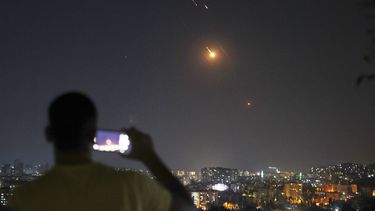 Un hombre toma una foto con su teléfono móvil mientras misiles lanzados desde Irán hacia Israel sobrevuelan Damasco, Siria, la madrugada del miércoles 18 de junio de 2025. (AP Foto/Ghaith Alsayed)