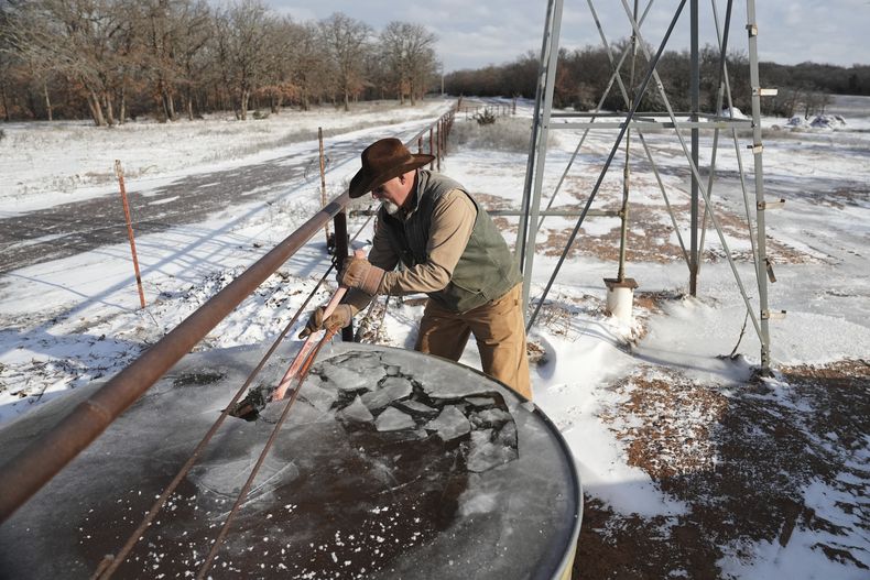 Walt Traywick utiliza un hacha para romper el agua congelada en un tanque de almacenamiento mientras trabaja en su granja, el miércoles 19 de febrero 2025, en Luther, Oklahoma. (AP Foto/Joshua A. Bickel)