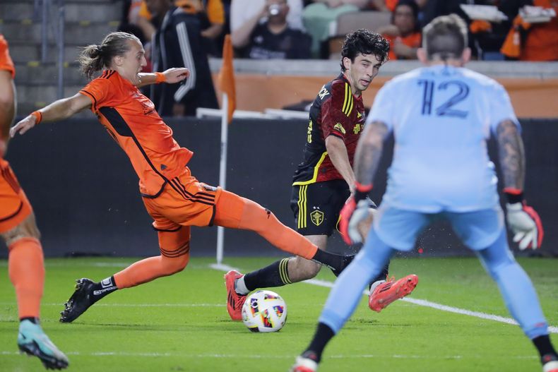 El mediocampista del Houston Dynamo, Griffin Dorsey, a la izquierda, intenta bloquear un tiro de gol del mediocampista del Seattle Sounders, Paul Rothrock, al centro, mientras el portero del Dynamo, Steve Clark (12), se coloca en el área durante la primera mitad del Juego 2 de la primera ronda de los playoffs de fútbol de la Copa MLS, el domingo 3 de noviembre de 2024, en Houston. (AP Foto/Michael Wyke)