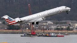 Mientras un avión de American Eagle despega, cuadrillas realizan tareas de recuperación cerca del punto en el río Potomac donde cayeron los restos de un avión comercial y un helicóptero militar que chocaron en pleno vuelo en el Aeropuerto Nacional Ronald Reagan, el jueves 6 de febrero de 2025, en Arlington, Virginia. (AP Foto/José Luis Magaña)